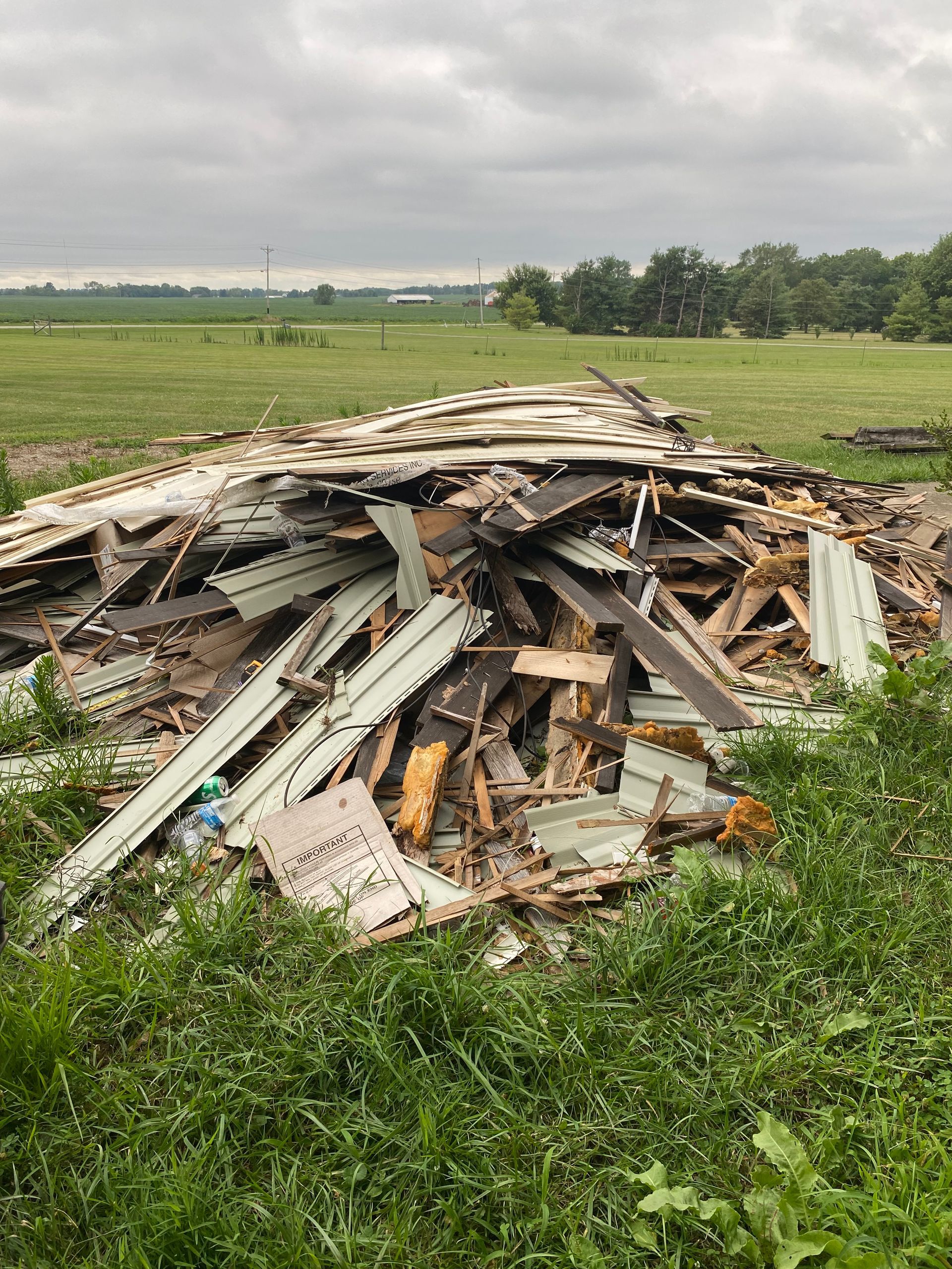 Pile of scrap wood and debris in a grassy field under an overcast sky