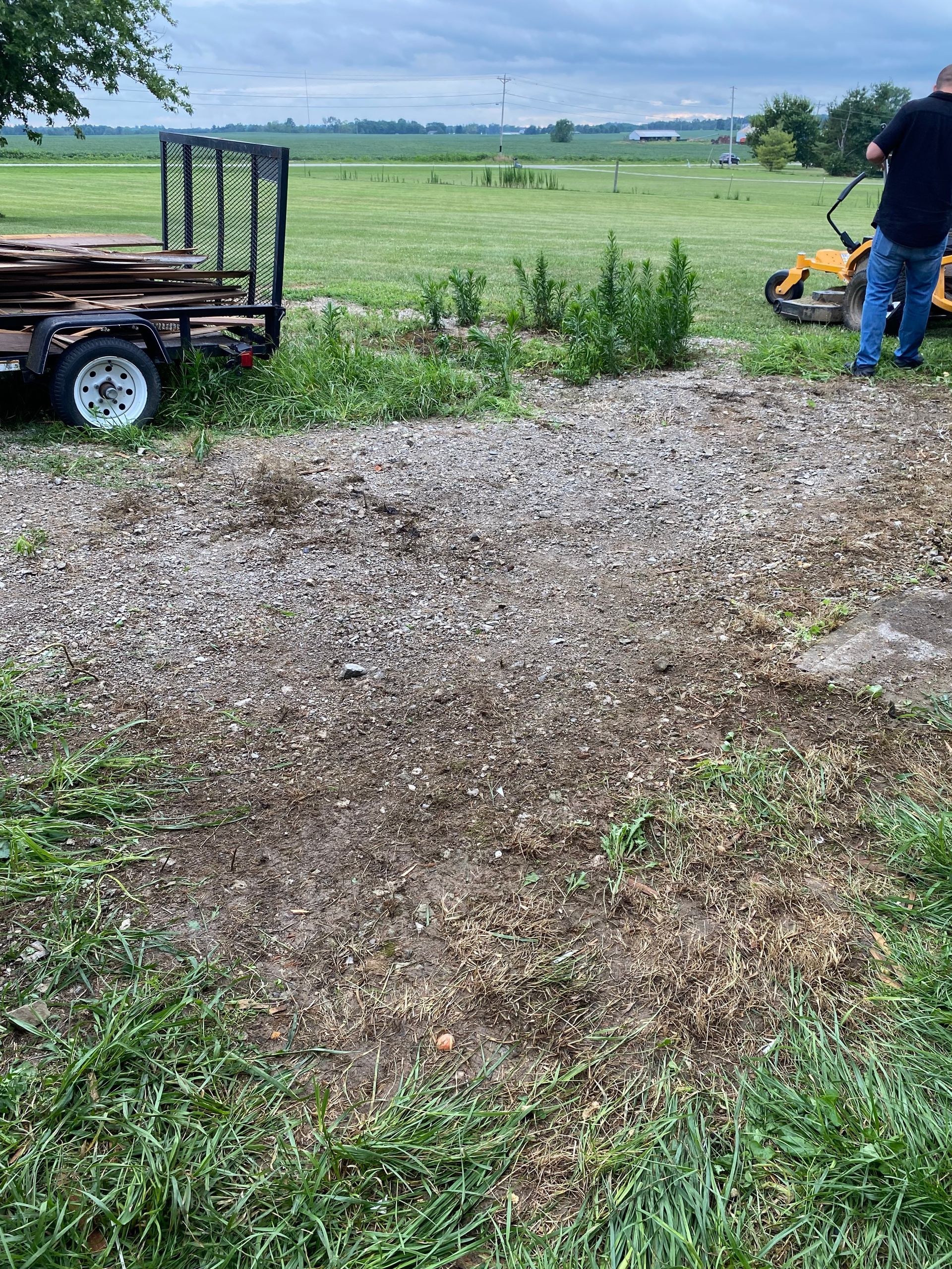 Person standing by a yellow machine near a gravel path and grassy field under cloudy skies